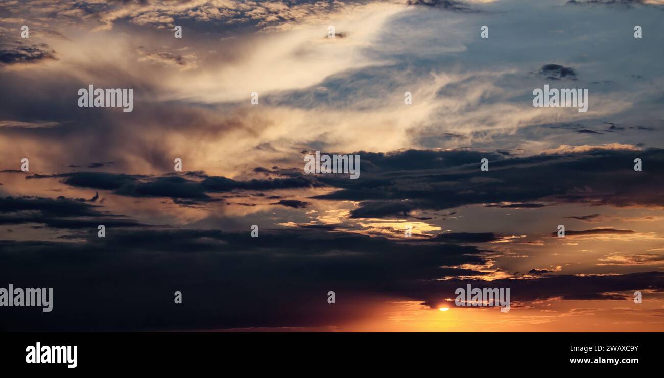The sky filled with dark clouds and a shining sun at sunset. Stock Photo