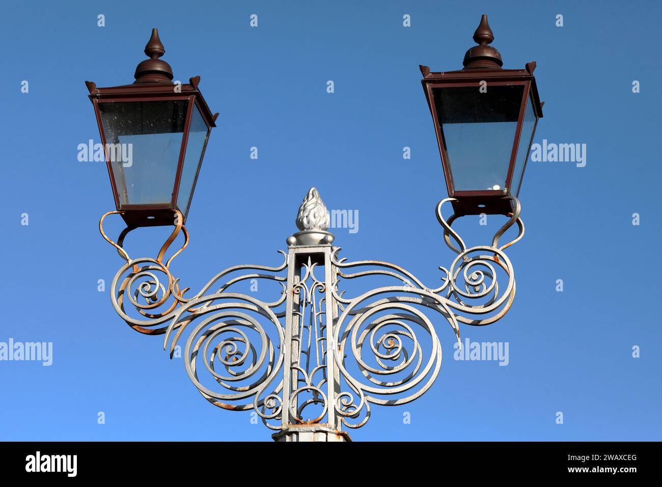 A double period lamp, the head detail from a lighting column with ornate scrolling metalwork Stock Photo