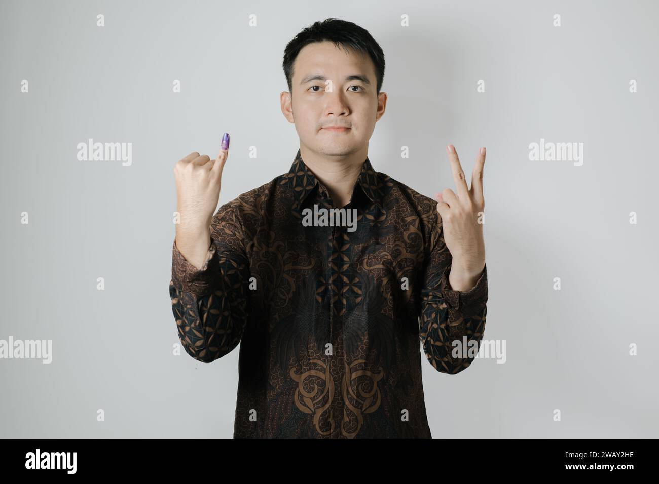 Asian man wearing Batik cloth is showing his little finger with purple ink applied and to choose number two after Pemilu or Indonesian election day Stock Photo