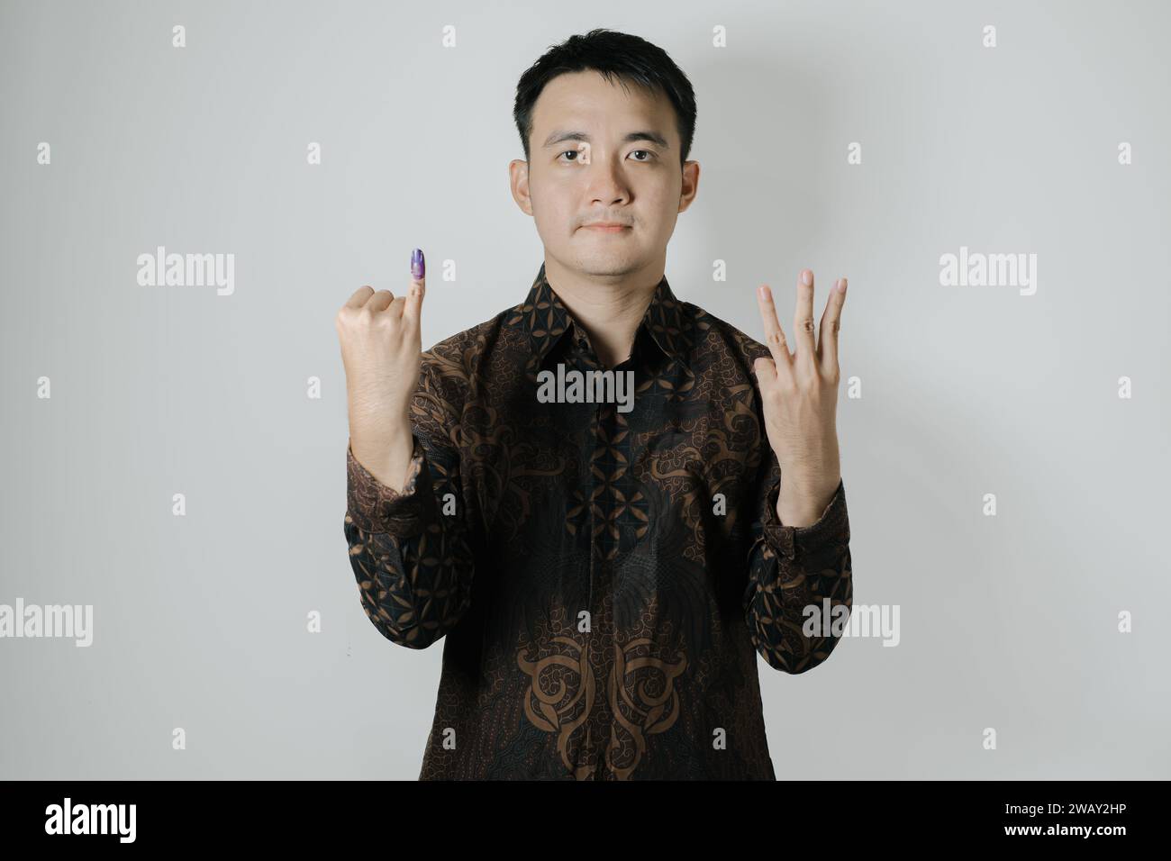 Asian man wearing Batik cloth is showing his little finger with purple ink applied and to choose number three after Pemilu or Indonesian election Stock Photo