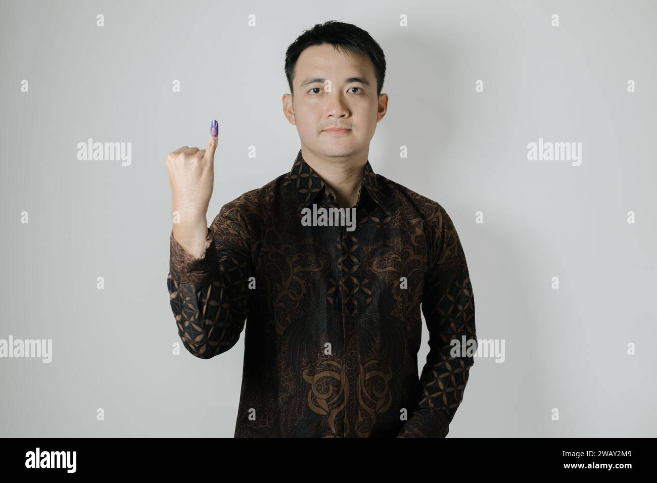 Asian man wearing Batik cloth is showing his little finger with purple ink applied after Pemilu or Indonesian presidential election Stock Photo