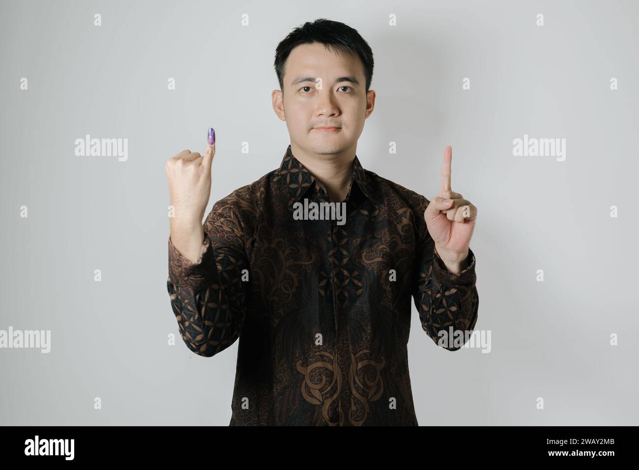 Asian man wearing Batik cloth is showing his little finger with purple ink applied and to choose number one after Pemilu or Indonesian election day Stock Photo