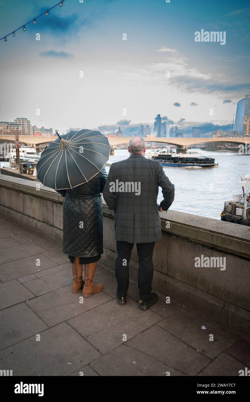 A stylish couple with an ornate umbrella enjoy the views over the River Thames in Westminster, Central London in England UK Stock Photo
