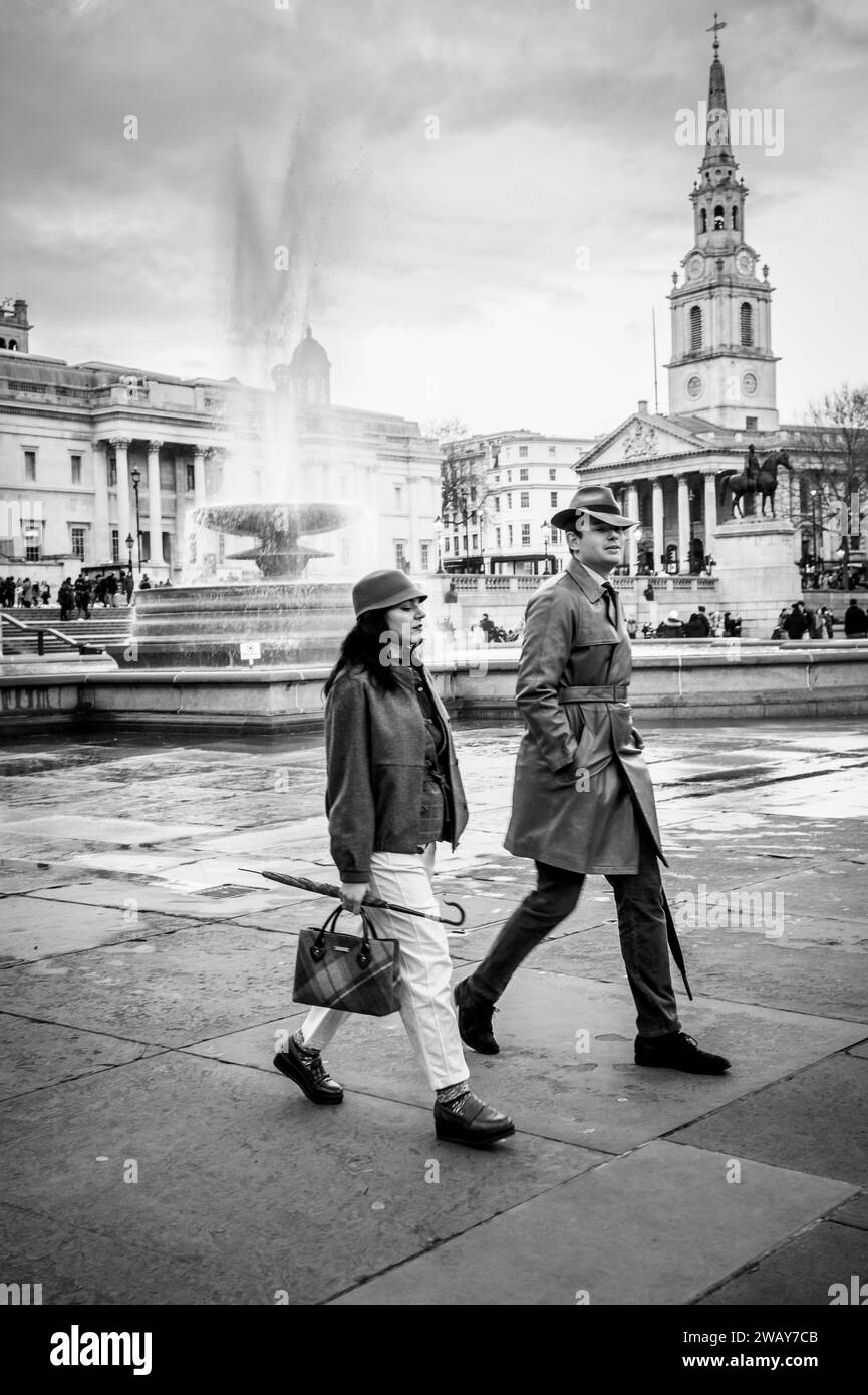 A well dressed young couple walk through Trafalgar Square in London
