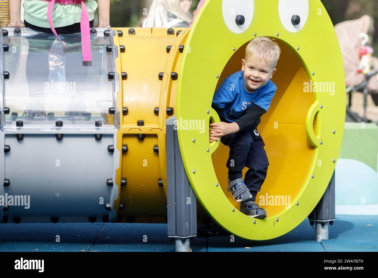 A cheerful boy in a blue blazer is playing active sports games in a yellow pipe obstacle course on the playground. Stock Photo