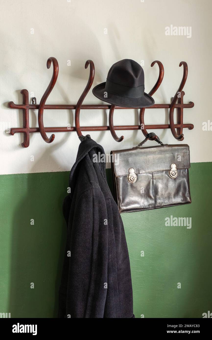 Black ancient leather briefcase, black hat and coat on the vintage wooden cloth hanger. The wall is half painted with green paint. Vertical photo. Stock Photo