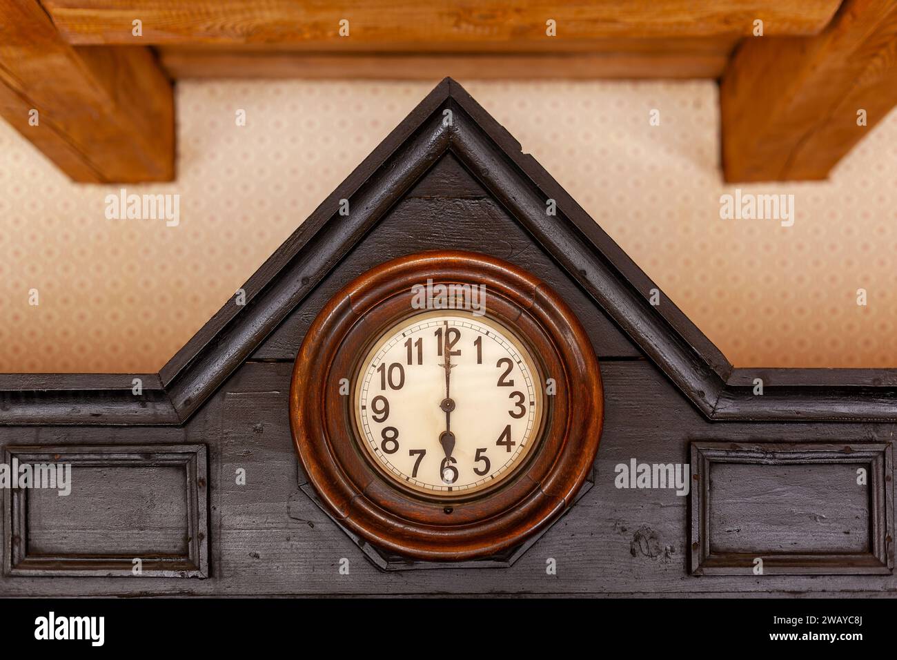 An antique German clock with a yellowed face is built into a roof-shaped brown wood cabinet. Stock Photo