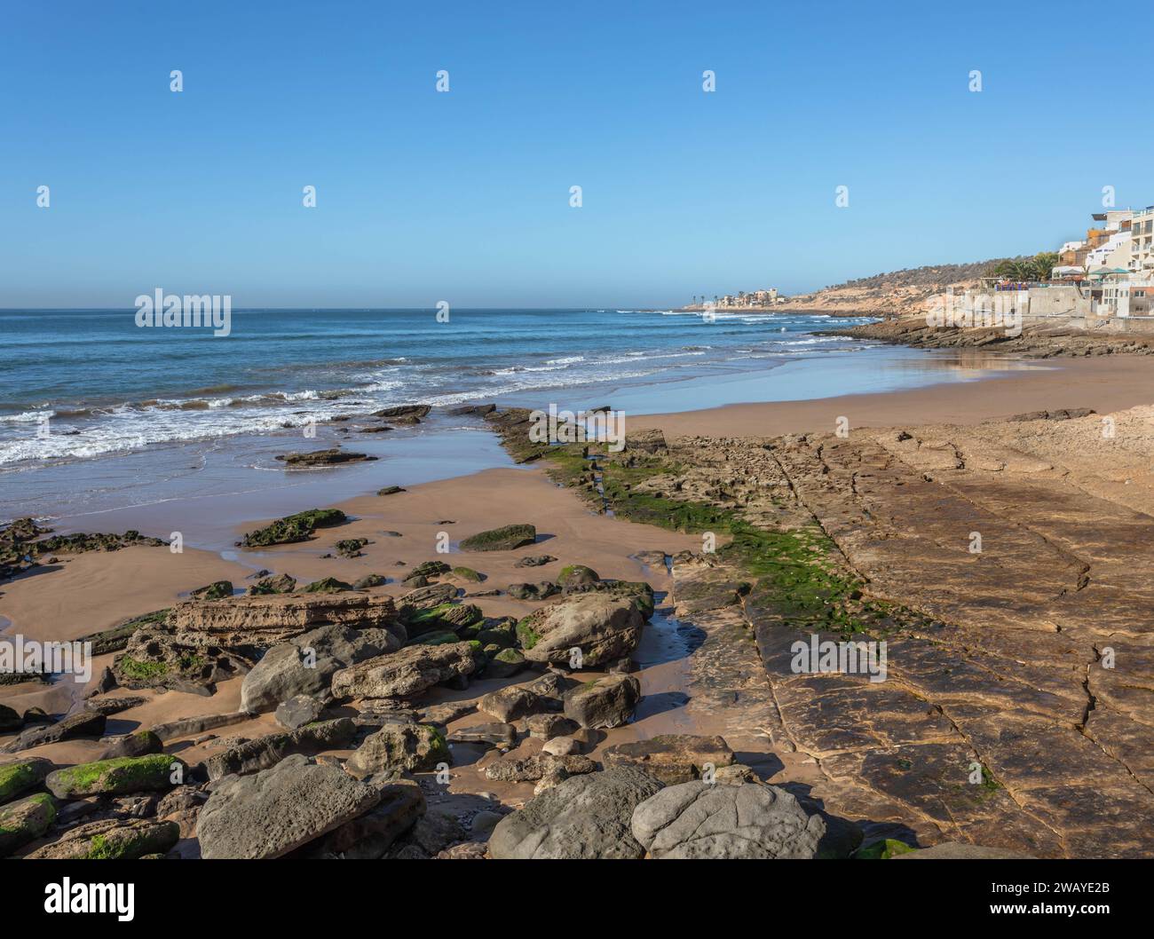 A wide-angle view of a bay in Taghazout, near Agadir, with sandy and rocky beach overlooking the Atlantic Ocean Stock Photo