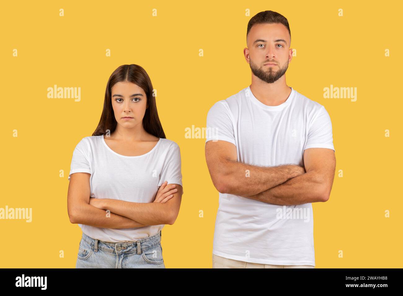 Stern-faced young couple with arms crossed in white t-shirts, exuding a strong sense of disagreement Stock Photo