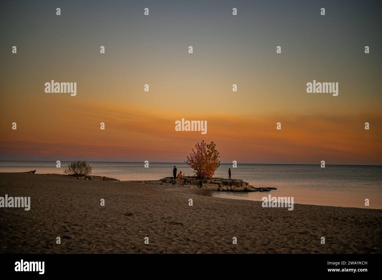 Three adults walking along a sandy beach at dusk, enjoying the warm summer weather Stock Photo