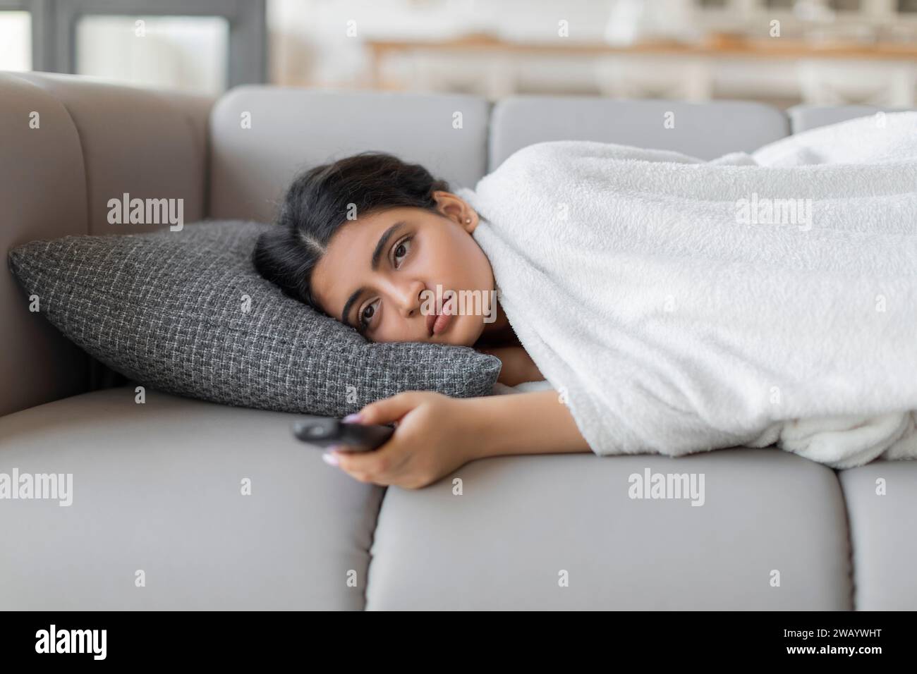 Bored indian woman with remote controller lying on sofa at home Stock Photo