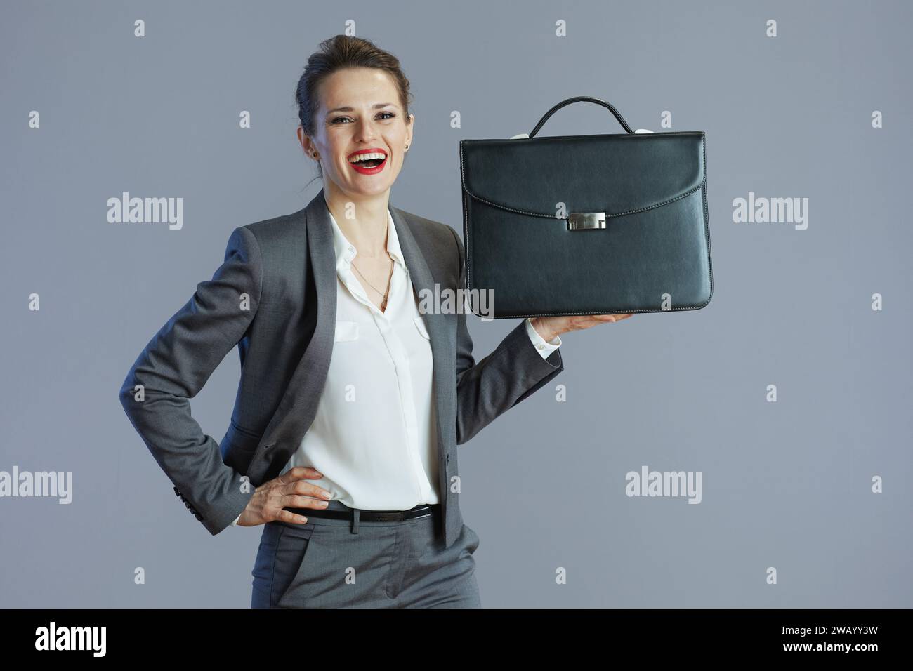 smiling elegant small business owner woman in grey suit with briefcase against gray background. Stock Photo