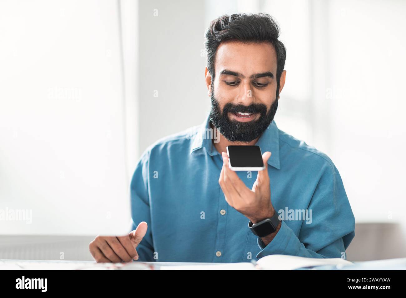 Hindu businessman with beard using voice assistant on phone Stock Photo