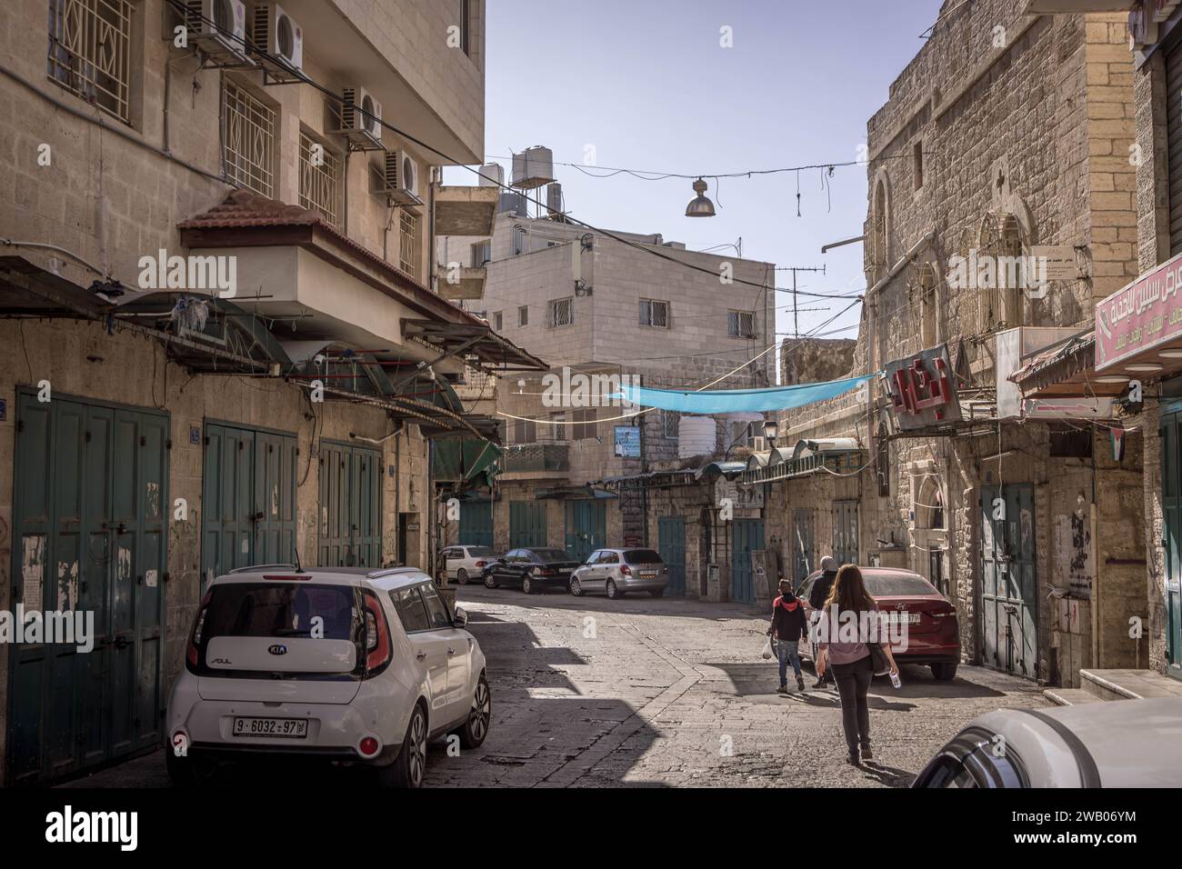 The narrow alley at the old part of Bethlehem city in Palestinian West Bank (Palestine) with Palestinian people passing by the closed shops. Stock Photo