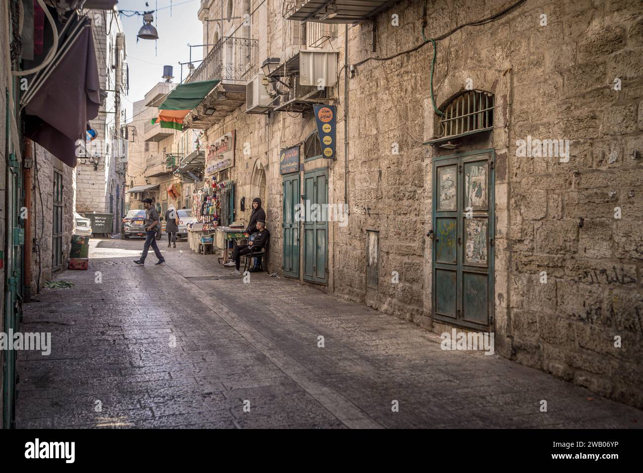 The narrow alley at the old part of Bethlehem city in Palestinian West Bank (Palestine) with Palestinian people passing by the closed shops. Stock Photo