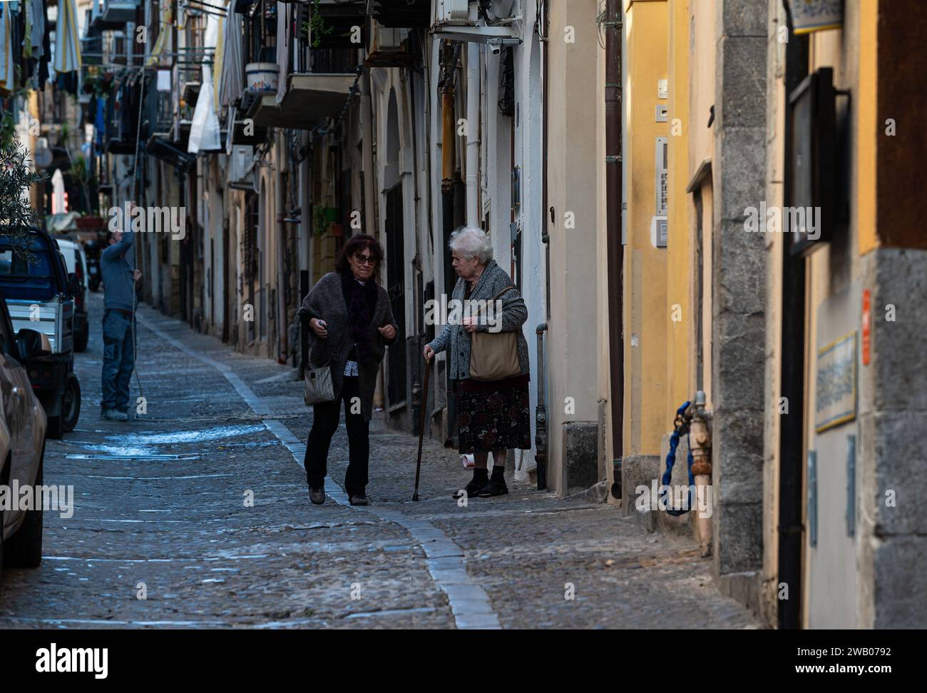 Cefalu, Sicily, Italy, December 19, 2023 - Old ladies talking in front of their houses in a narrow alley Stock Photo