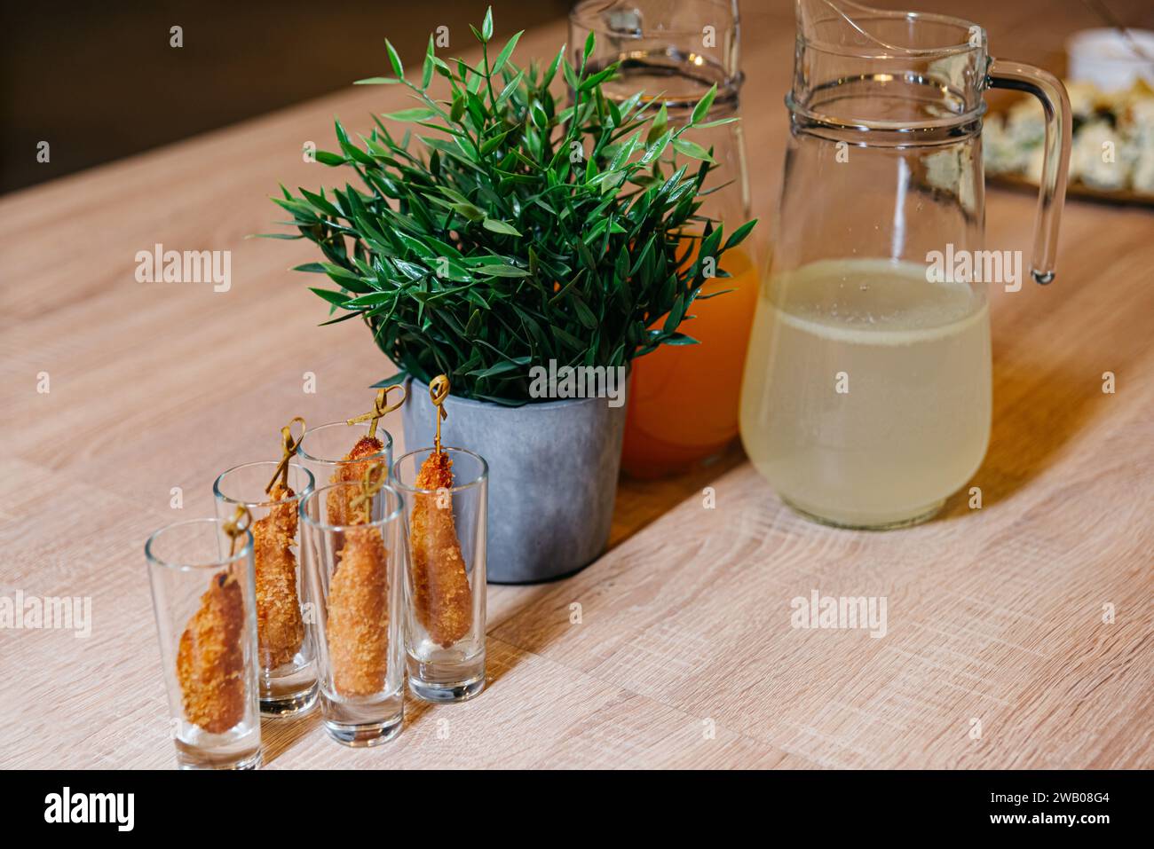 A wooden table topped with appetizers in glasses and jugs filled with liquids and lemonades Stock Photo