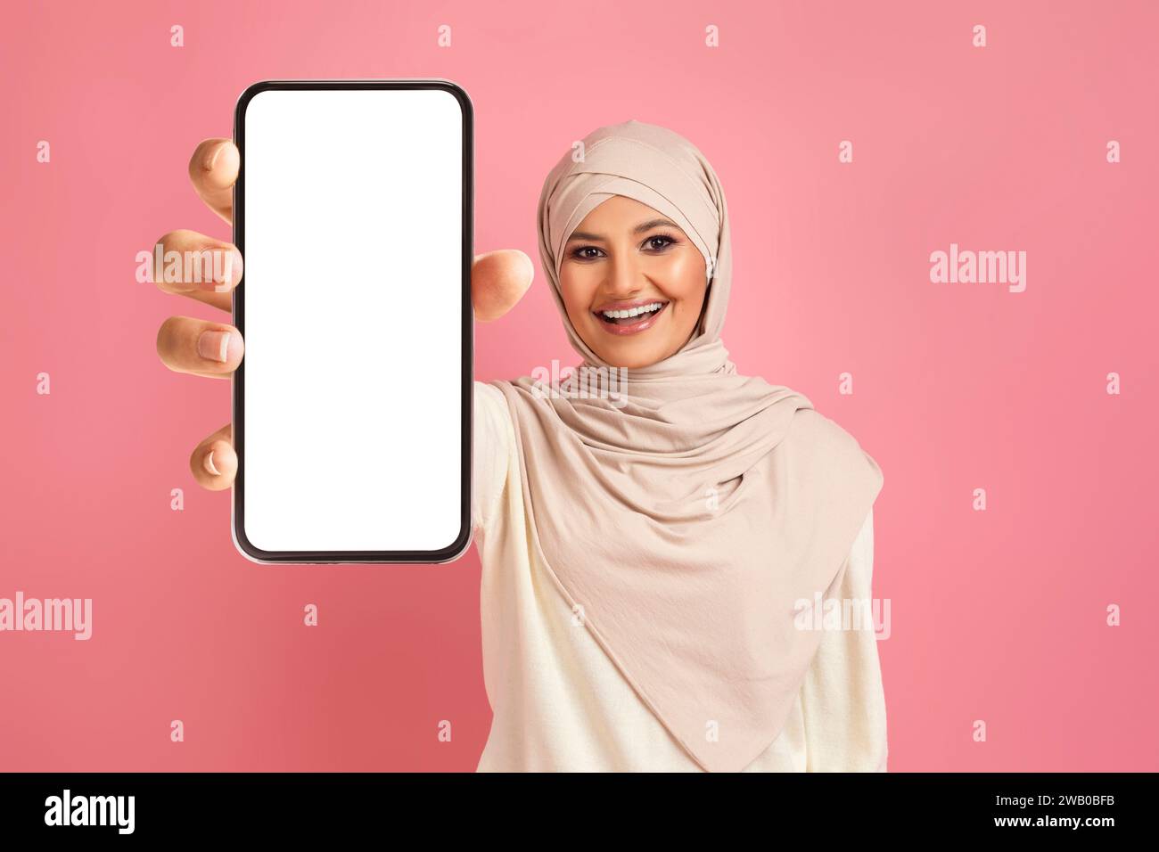 Cheerful arab muslim woman in hijab displaying smartphone with blank ...