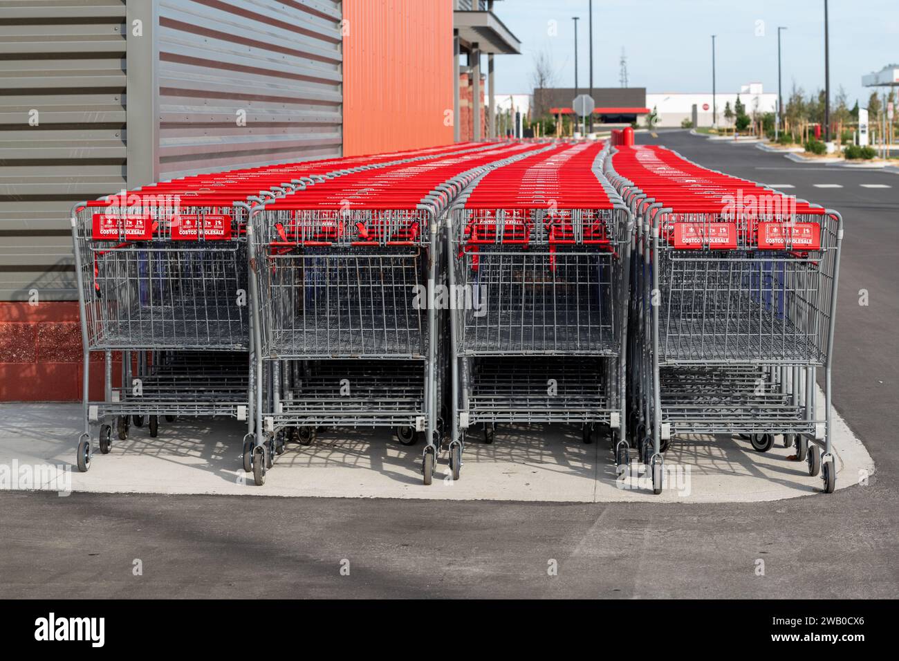 Rows of new metal Costco shopping carts with red handles. The retail pushcarts are in front of an orange and grey colored metal outside wall of a shop Stock Photo