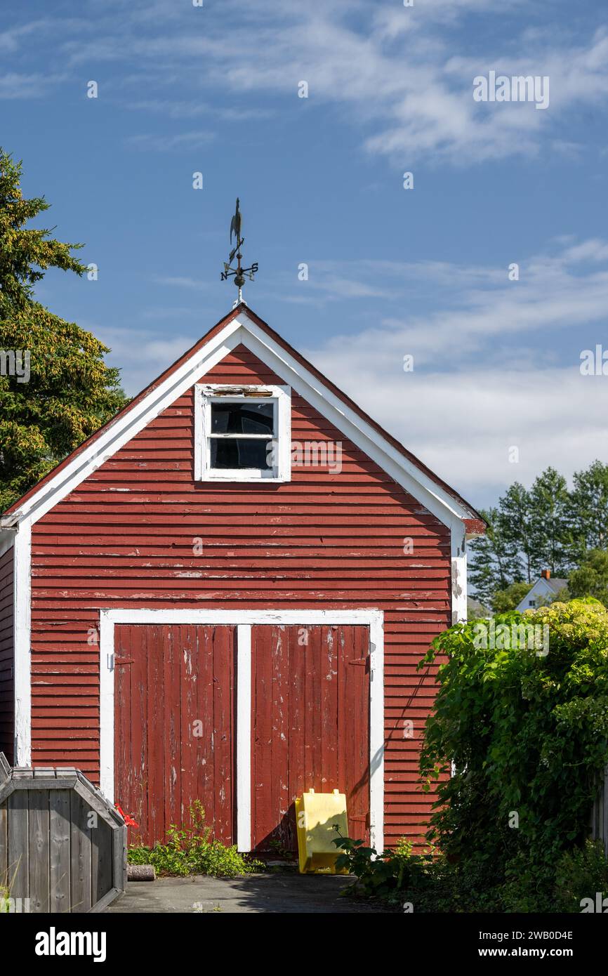 The peaked roof section of a vintage red barn. The wooden structure is painted vibrant red with white trim. There's a small hayloft door and two barn Stock Photo