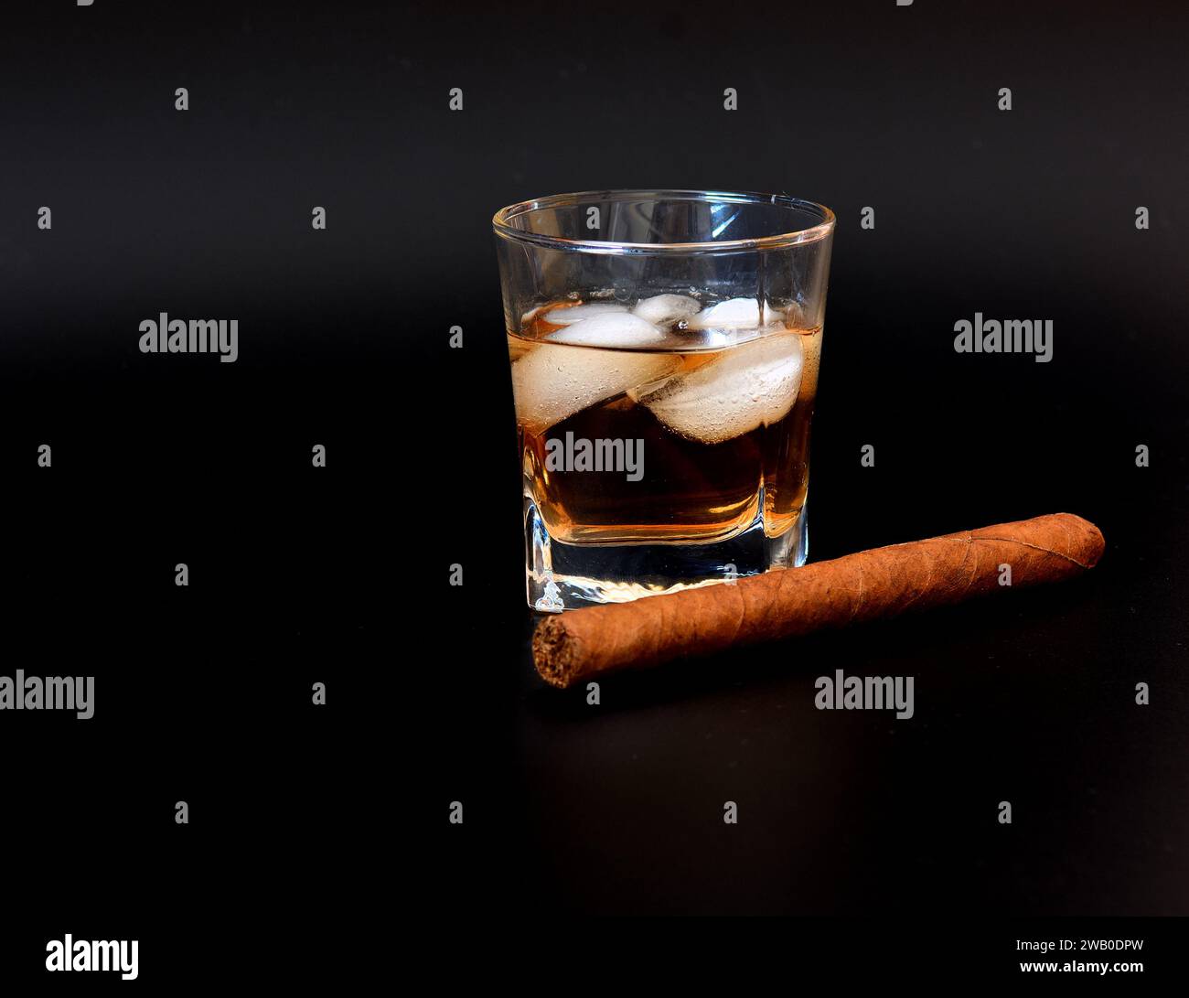 Cuban cigar and glass of whiskey with ice on a black background. Close-up. Stock Photo
