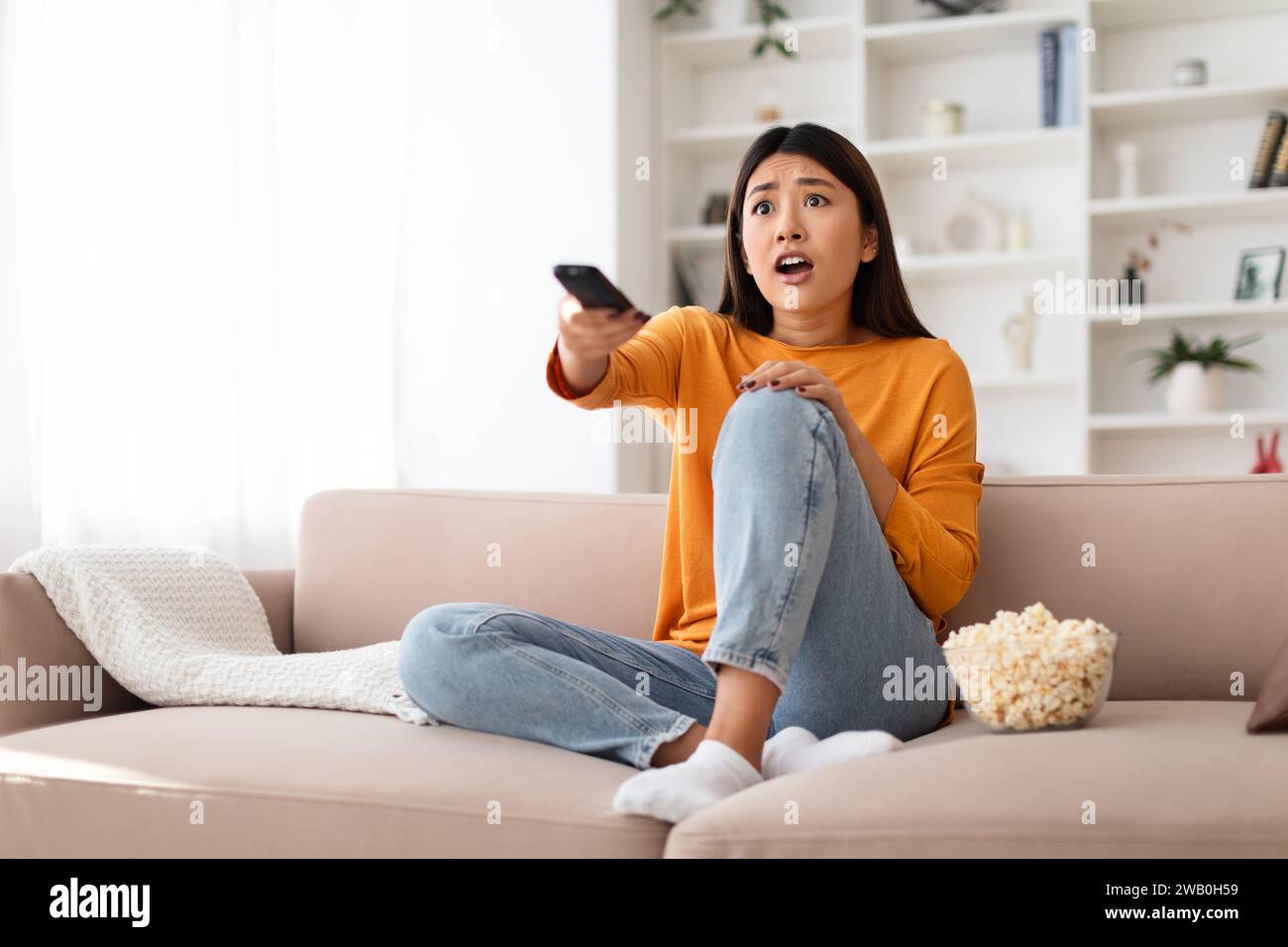 Shocked millennial asian woman watching TV at home Stock Photo