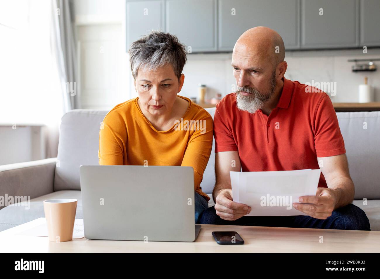 Senior Spouses Reading Papers And Using Laptop Computer At Home Stock Photo