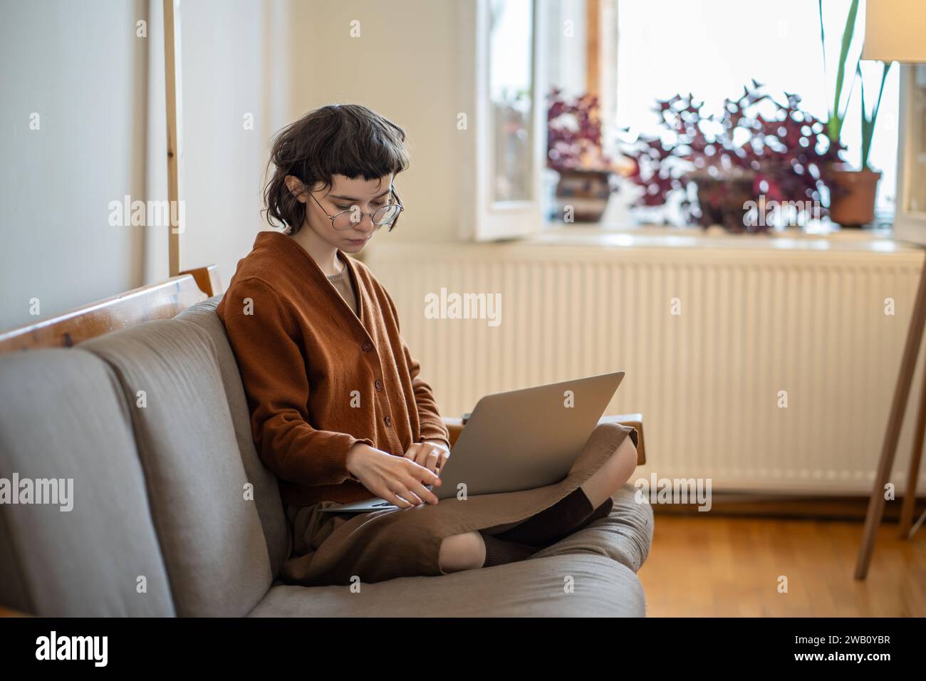 Focused student girl teenager studying on laptop sitting on couch at home. Self-education.  Stock Photo