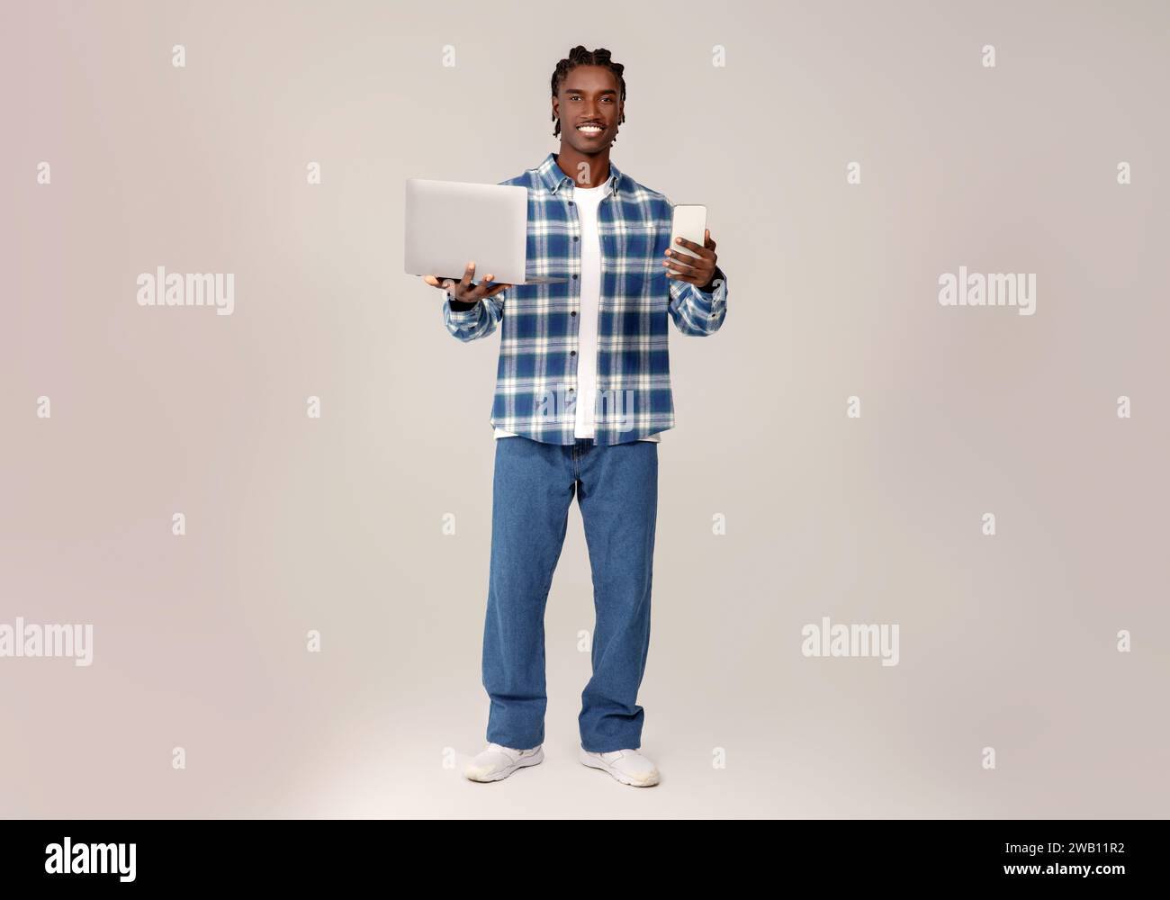 Multitasking young black man holding laptop and smartphone in hands Stock Photo