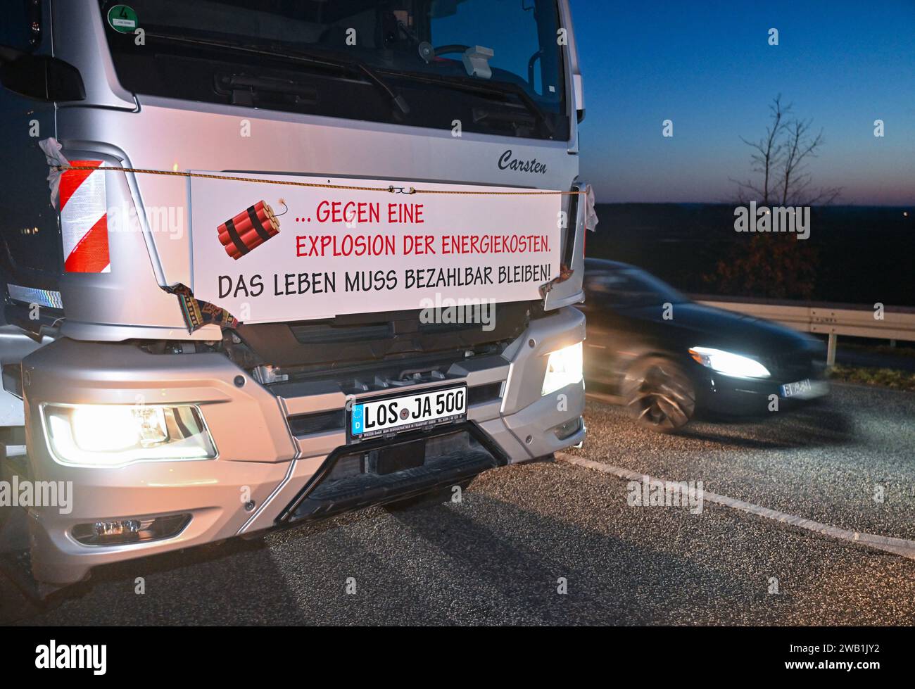 Jacobsdorf, Germany. 08th Jan, 2024. A haulage contractor blocks the entrance to the A12 highway towards Berlin with his truck and has a poster with the words 'Against an explosion in energy costs. Life must remain affordable!' attached to his vehicle. In response to the federal government's austerity plans, the farmers' association has called for a week of action with rallies and rallies starting on January 8. It is to culminate in a major demonstration in Berlin on January 15. Credit: Patrick Pleul/dpa/Alamy Live News Stock Photo