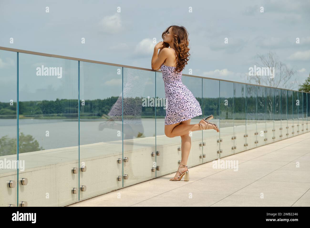 Slender woman in sundress with straps leans on glass railing of observation deck Stock Photo