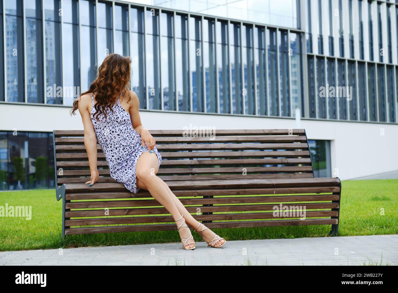 Unrecognizable woman with long slim legs in sandals on bench Stock Photo