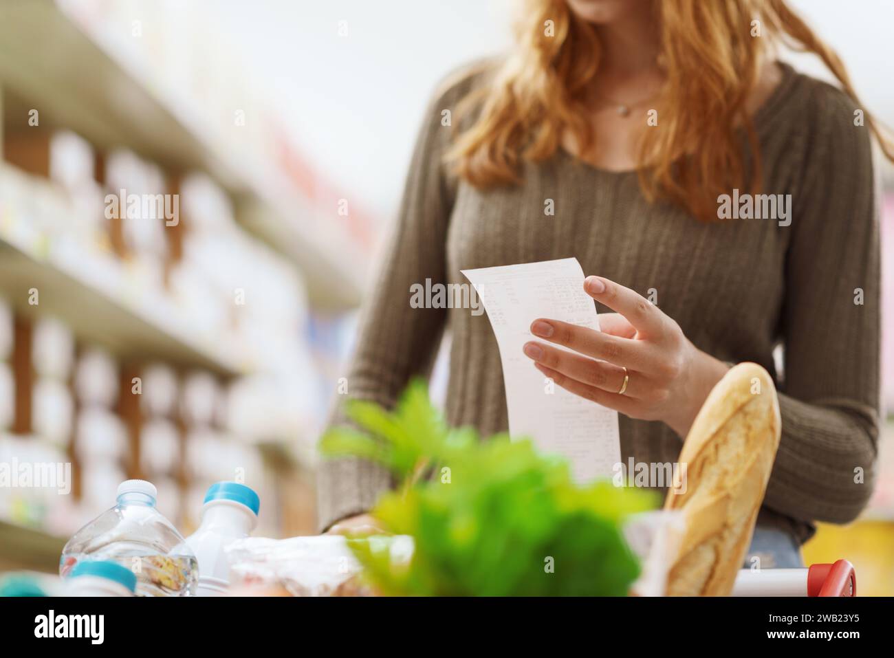 Woman pushing a full shopping cart at the supermarket and checking a ...