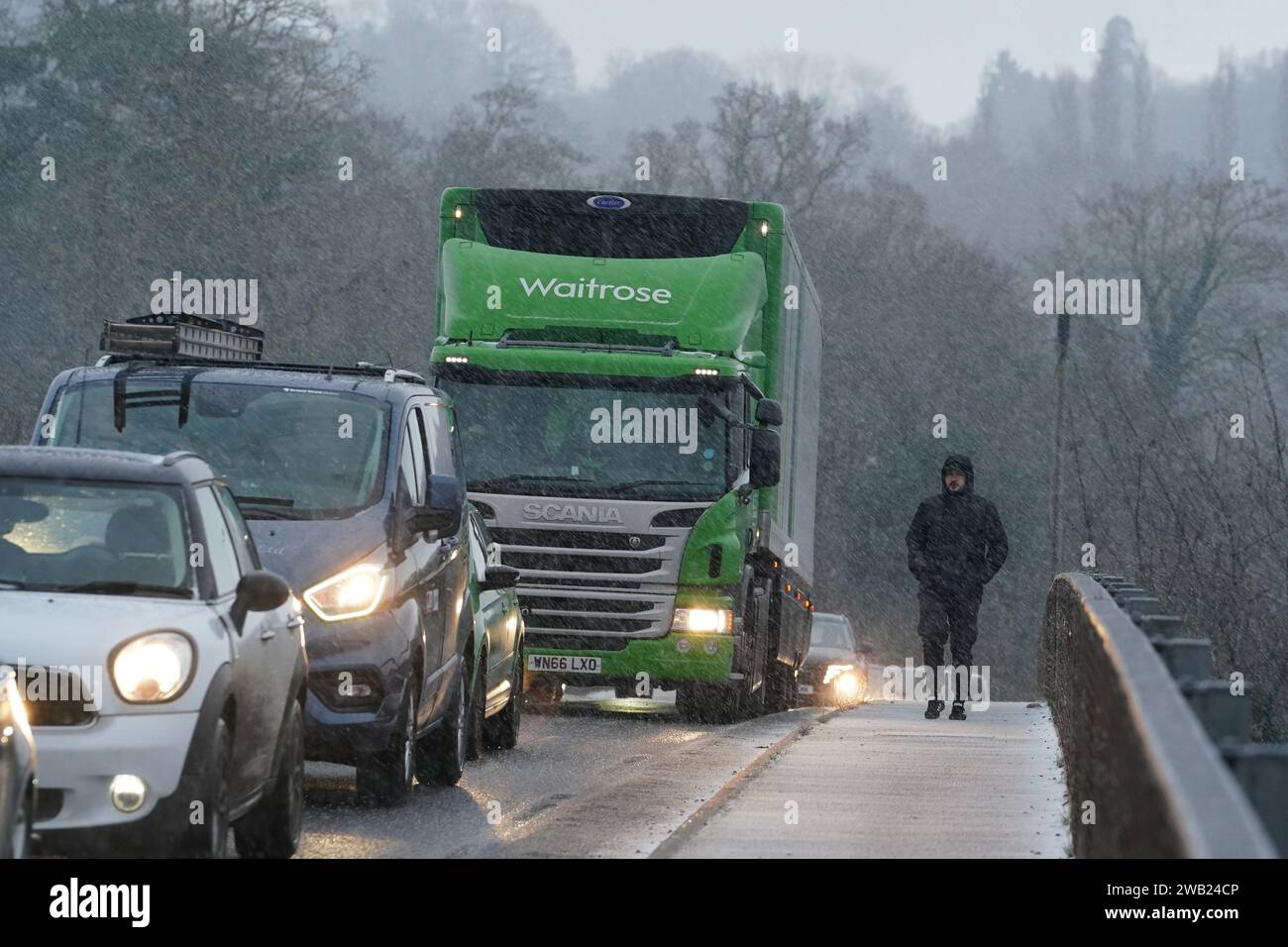 A pedestrian passes queuing vehicles on a motorway bridge as he walks through a snow shower near Maidstone in Kent. Sleet and snow showers have been forecast for parts of the country on Monday as some regions are still trying to grapple with flooding following intense rainfall. Picture date: Monday January 8, 2024. Stock Photo