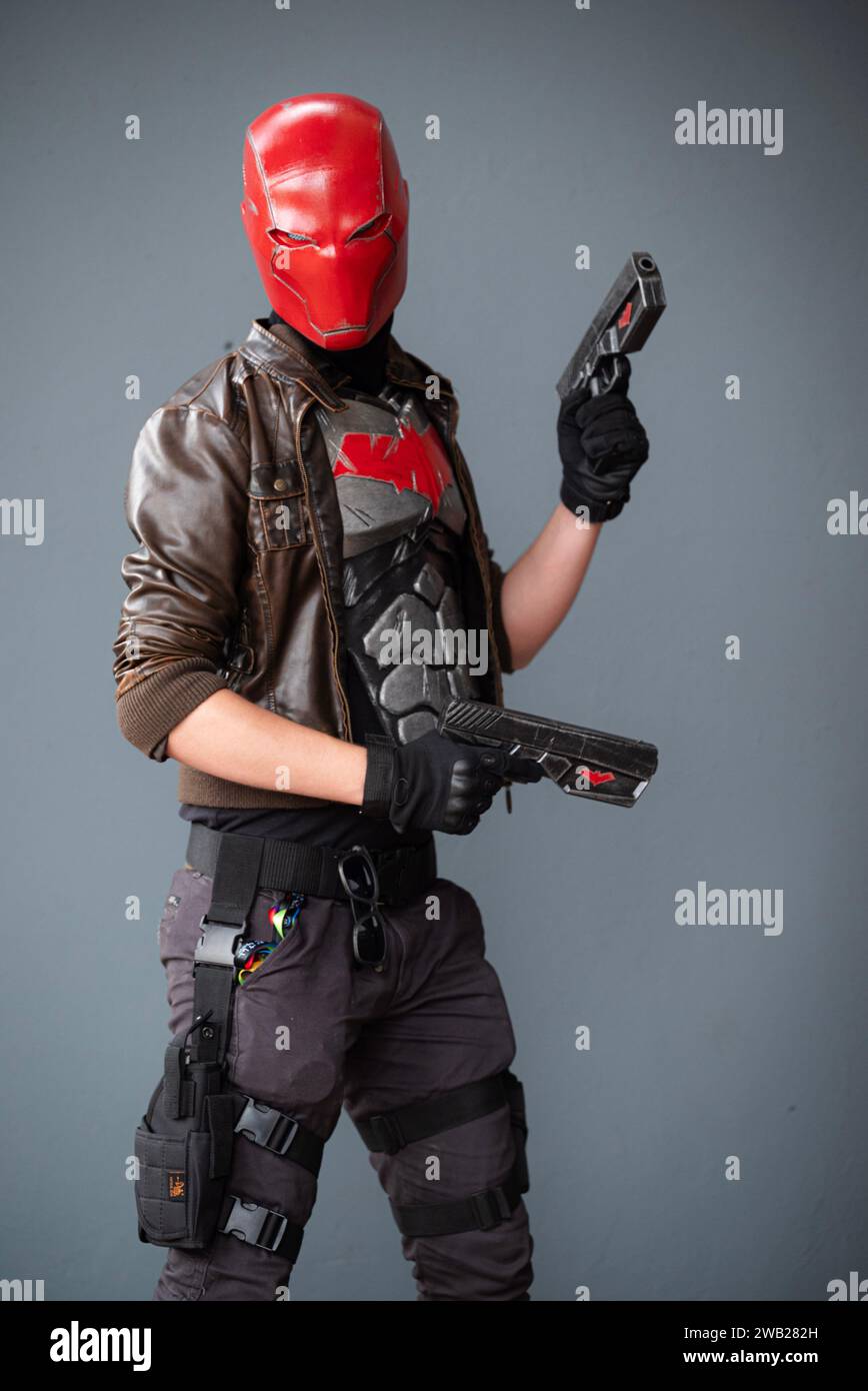 A male cosplayer in a costume with a red helmet, leather jacket, and