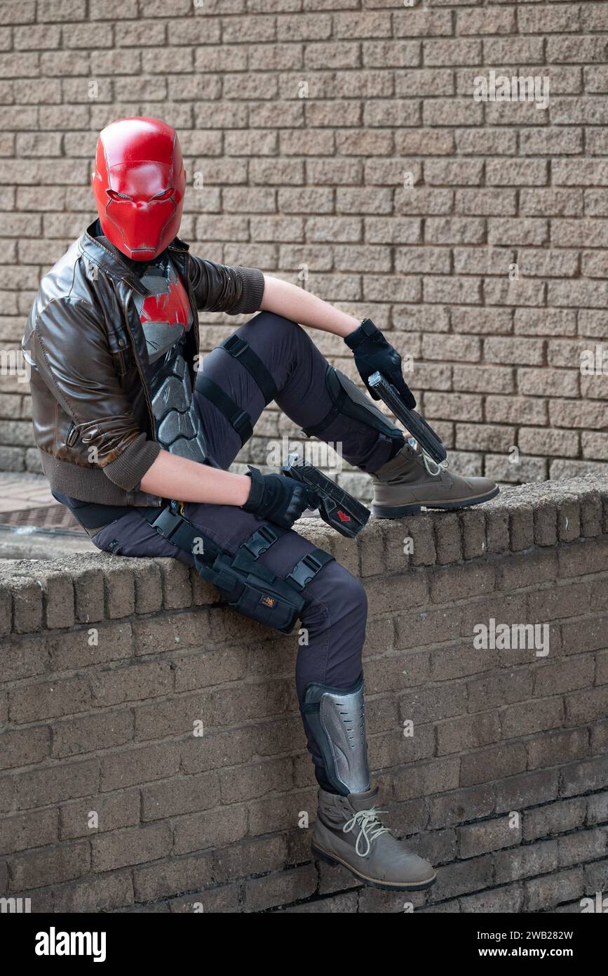 A male cosplayer in a costume with a red helmet, leather jacket, and