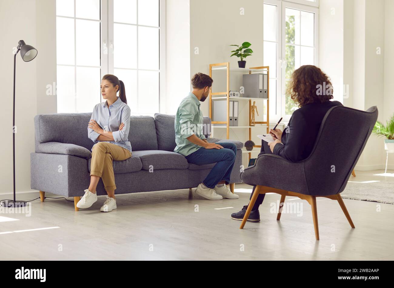 Couple sitting on opposite sides of sofa ignoring each other at family psychologist office. Stock Photo