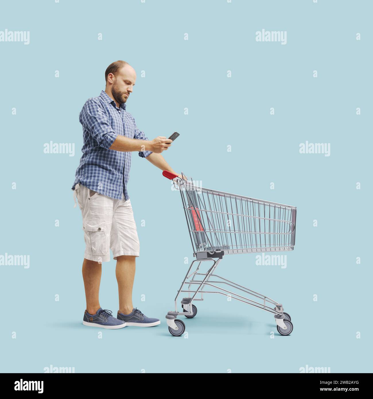Man using his smartphone and pushing a trolley, grocery shopping ...