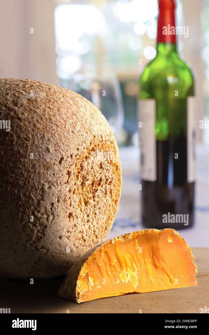 Close up shot of aged mimolette cheese with a bottle of red wine in the background. Stock Photo