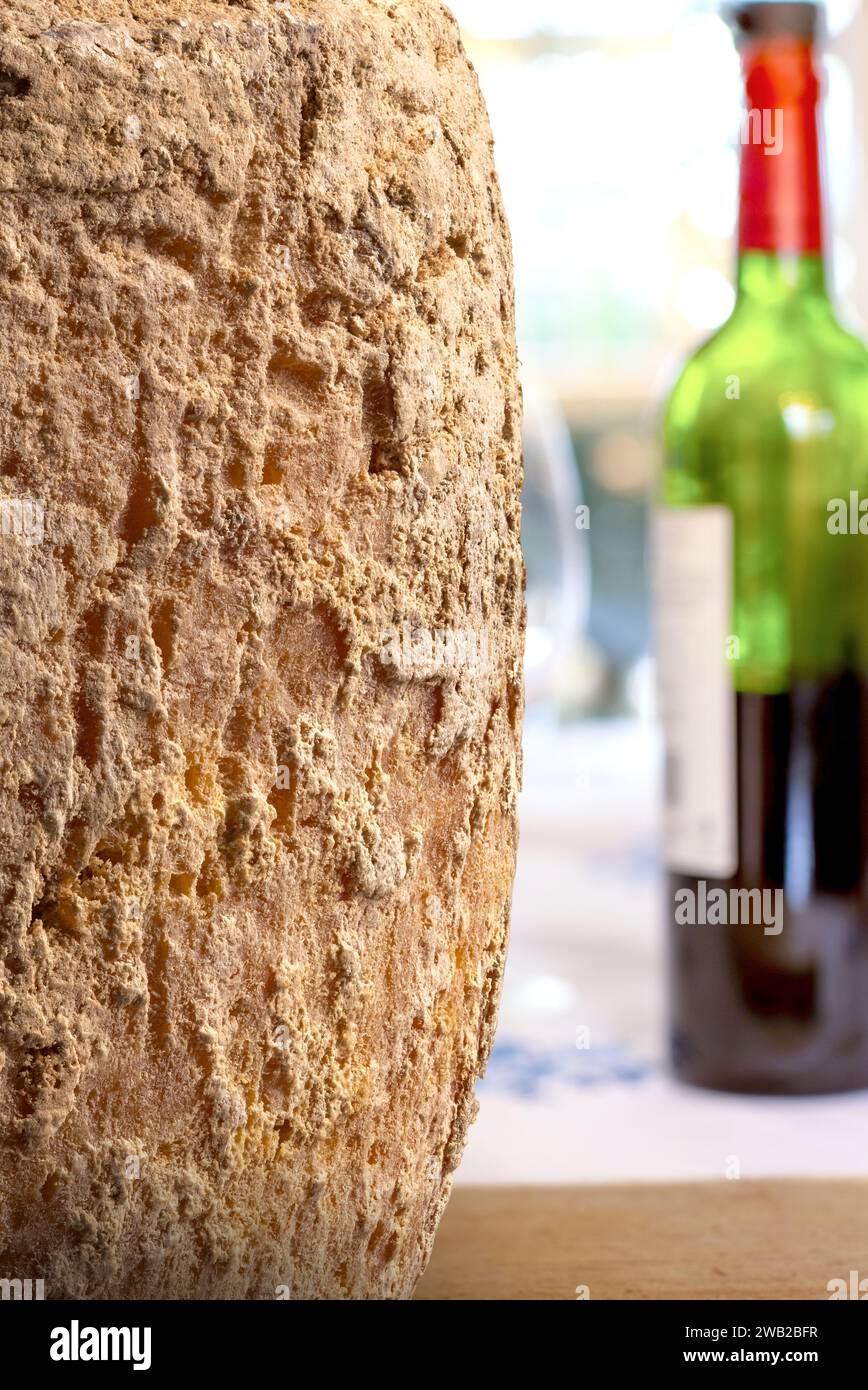 Close up shot of aged mimolette cheese with a bottle of red wine in the background. Stock Photo
