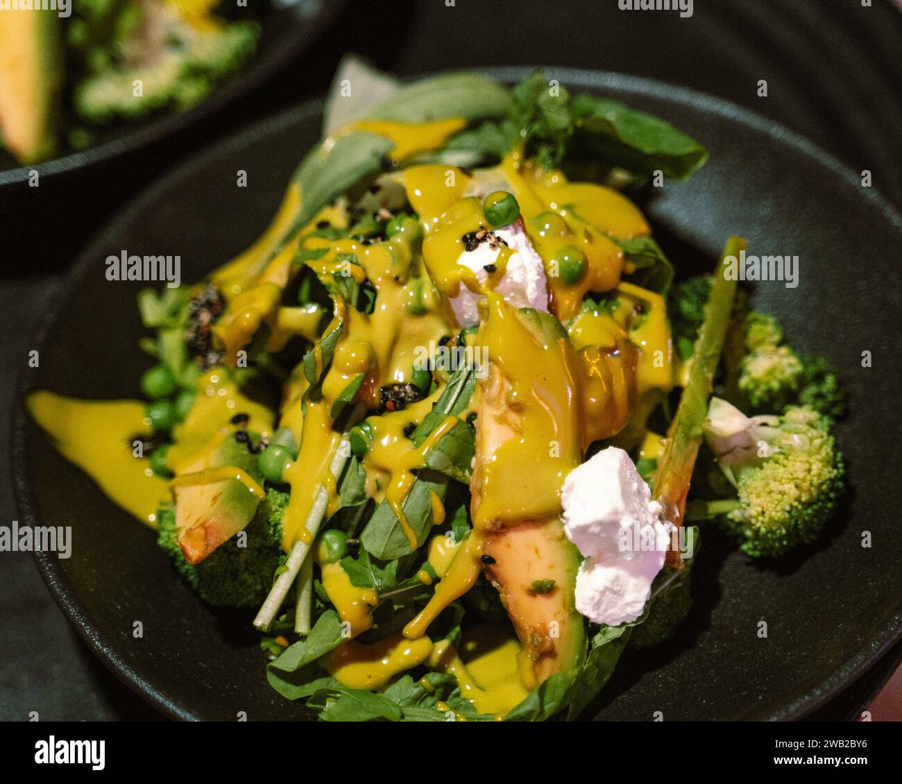 A delicious plate of food consisting of broccoli, onions, and cheese, served on a black plate Stock Photo