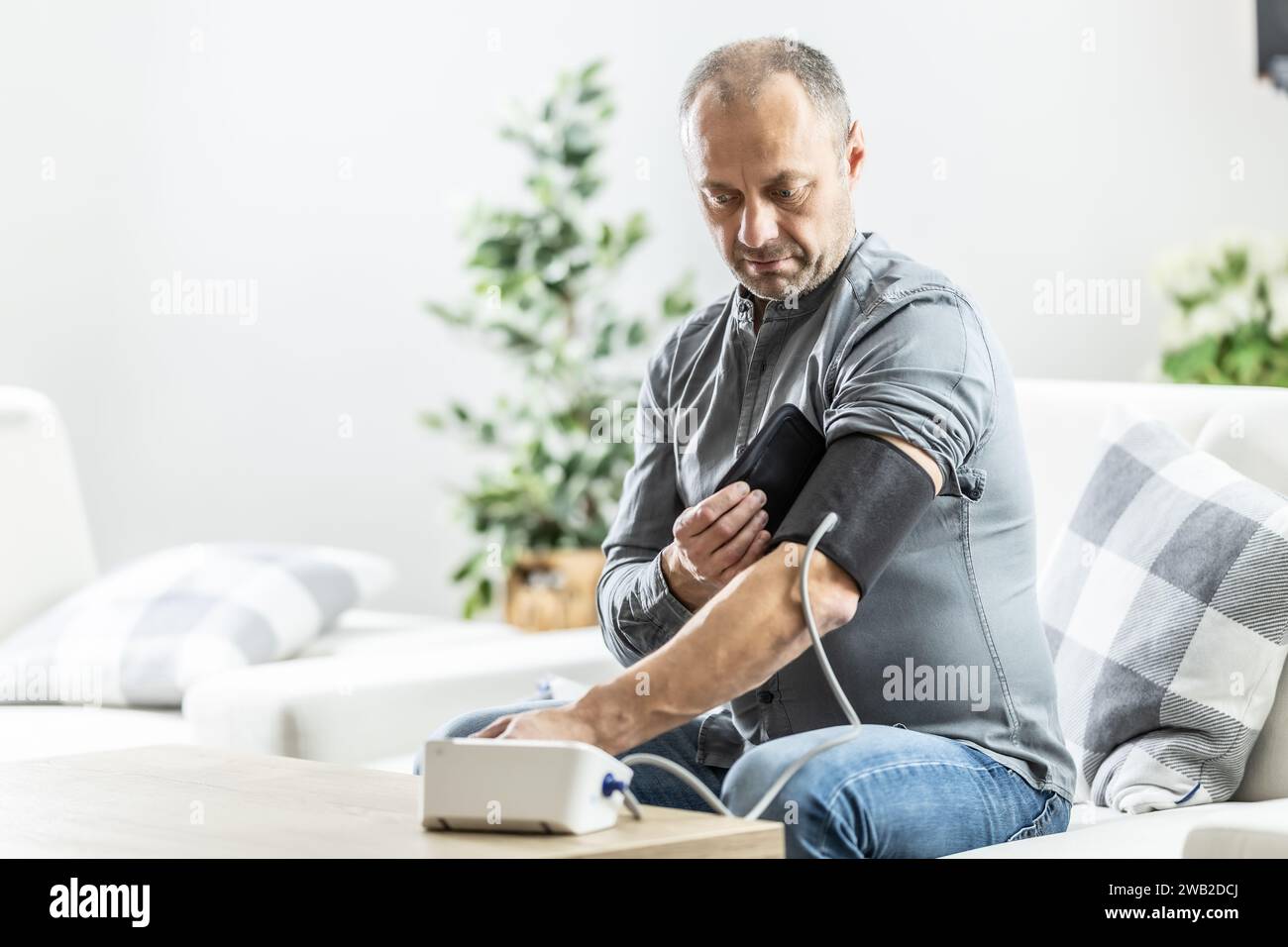 A mature man checking his blood pressure with a digital blood pressure monitor at home. Stock Photo