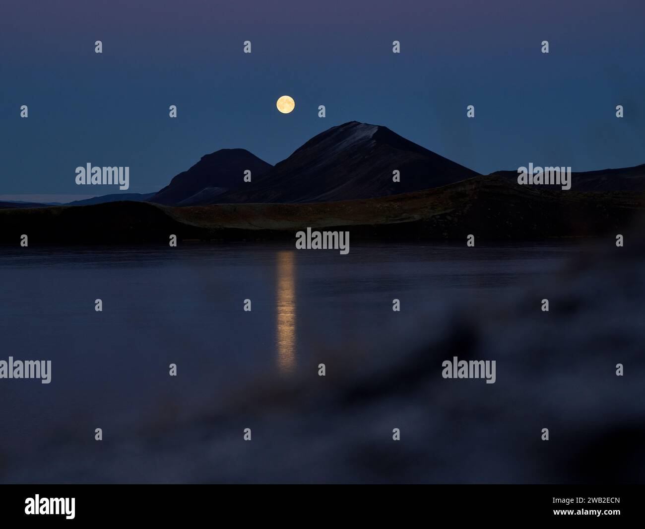 Scenic moonrise on night sky over lake and mountains Stock Photo
