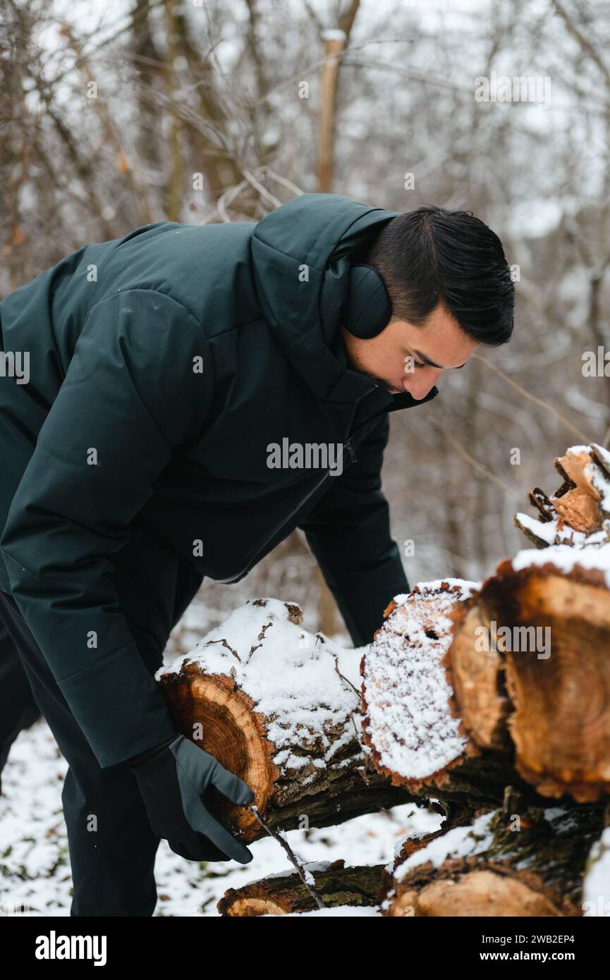Young man stacking wood logs in snowy weather to later use as firewood Stock Photo