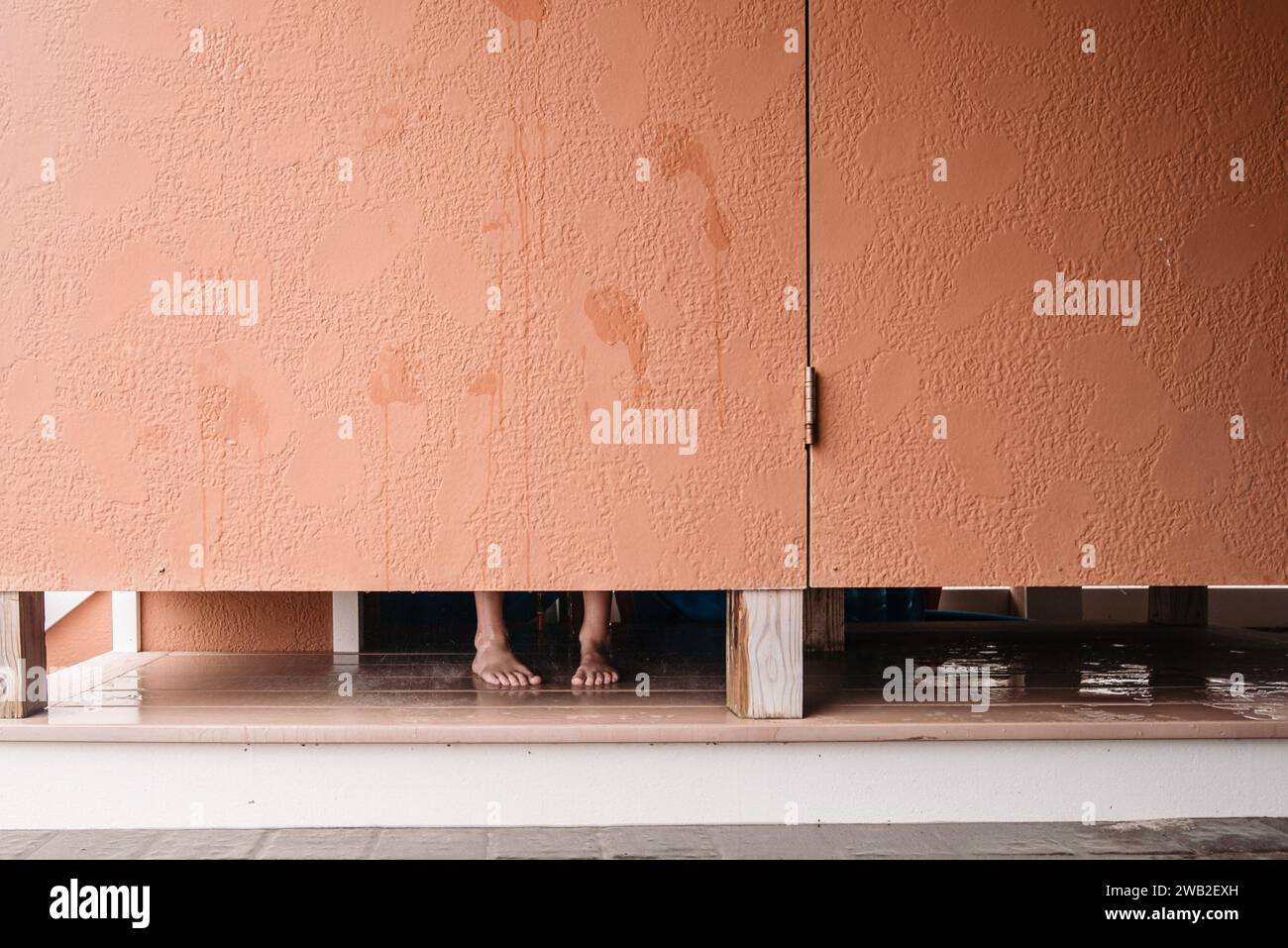 Feet visible under stall door of outdoor shower Stock Photo