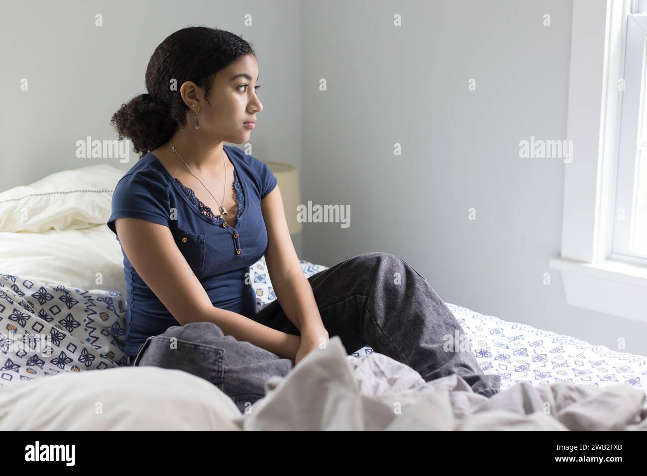 Biracial teen girl sits on un unmade bed looking depressed Stock Photo