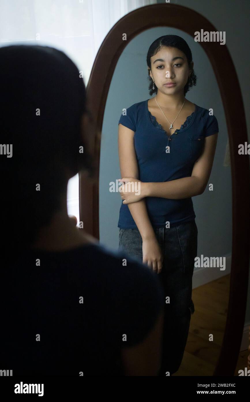 Biracial teen girl looks at herself critically in the mirror Stock Photo