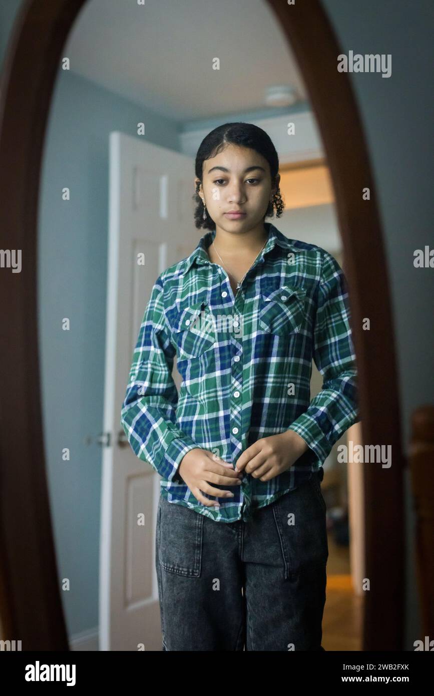 Biracial teen girl looks at herself critically in the mirror Stock Photo