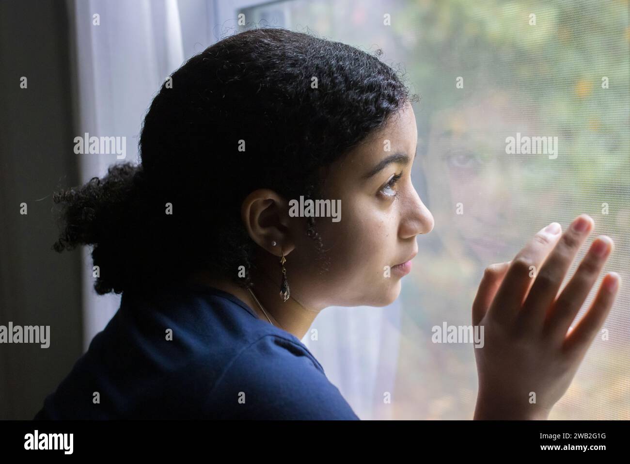 Biracial teen girl in profile looks out a window Stock Photo