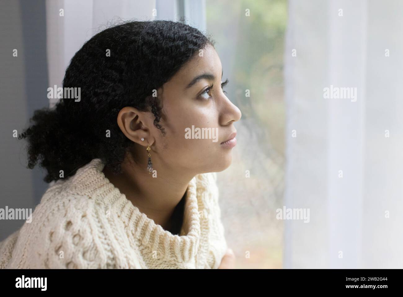 Biracial teen girl by window looking depressed Stock Photo